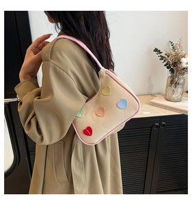 Dettaglio della borsa beige intrecciata con finiture in pelle rosa e toppe a cuore colorate