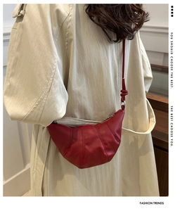 Close-up of bright red crescent bag with knotted strap worn over a beige trench coat