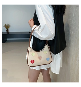 Dettaglio della borsa hobo intrecciata con toppe a cuore colorate sulla spalla del modello