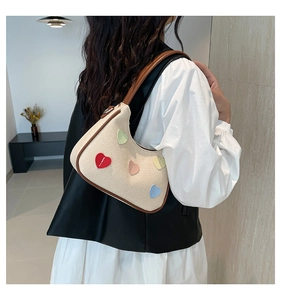 Dettaglio della borsa intrecciata beige con patch a cuore colorate e tracolla in pelle marrone