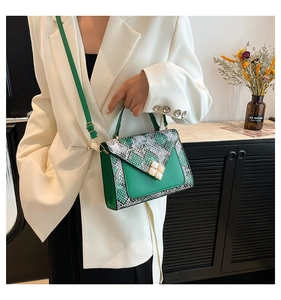Detail van groene handtas met slangenpatroon en gouden sluiting bij een witte blazer