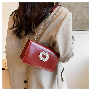Close-up of a red leather crossbody bag with sparkling diamond buckle and silver chain