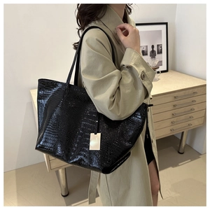 Detail of black crocodile pattern tote bag styled on model with trench coat for fashion look