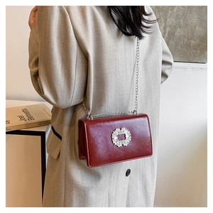Detail view of burgundy faux leather crossbody bag with rhinestone buckle and chain strap