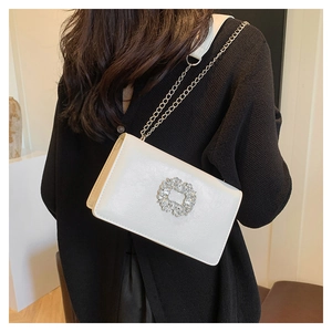 Close-up of white leather crossbody bag featuring a sparkling crystal buckle and chain