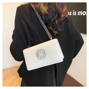 Detail of white glossy leather bag with sparkling rhinestone flower buckle and silver chain