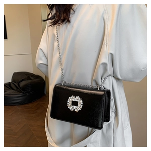 Detail of a black glossy crossbody bag with silver chain and luxury rhinestone buckle