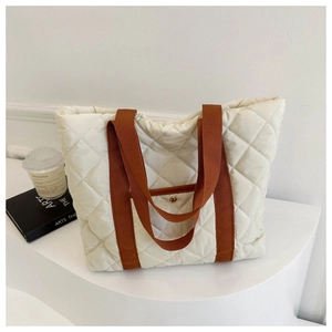 Detail of quilted tote bag with brown straps and gold button on minimal white platform