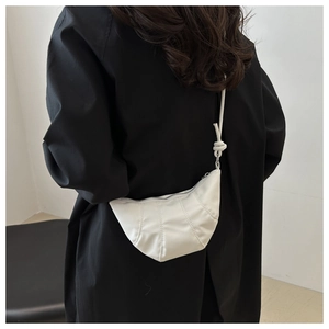 Detailed view of a white pleated croissant bag with knot detail worn by a model in black