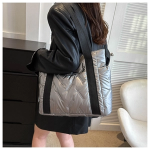 Silberne gesteppte Puffer-Tasche mit breitem schwarzem Gurt in der Seitenansicht am Model