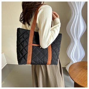 Detail of black quilted tote bag featuring orange straps and a front pocket with gold buckle