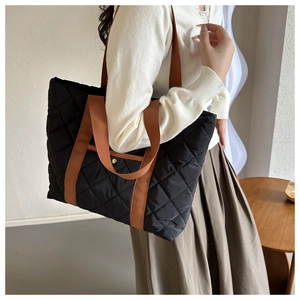 Detail of black quilted tote bag with brown straps and gold buckle in a lifestyle setting