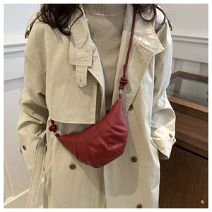 Detail of dark red croissant bag featuring textured stitching and side knot shoulder strap