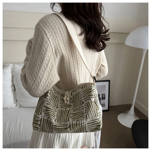 Detail of green striped woven tote bag with white shoulder strap and wavy texture