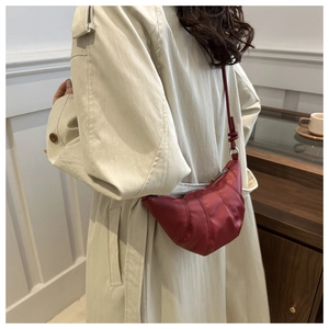 Detail of red crescent croissant bag with pleated design worn with a beige trench coat