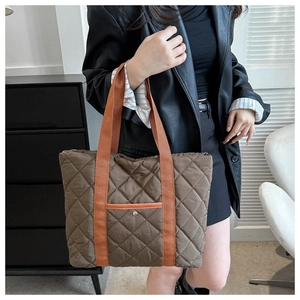 Detail of brown quilted tote bag with contrasting orange straps and front pocket