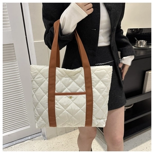 Detail view of cream quilted tote bag featuring brown straps and a golden snap button