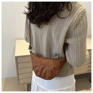 Detail of a brown crescent-shaped crossbody bag with knotted strap on a model shoulder