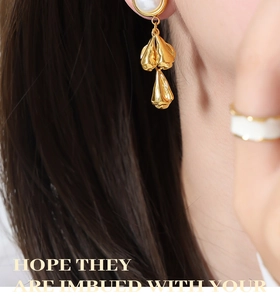 Detail of baroque pearl earrings with lava-textured gold pendants on a female model