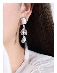 Detail of silver drop earrings featuring a lustrous pearl and textured metallic leaves