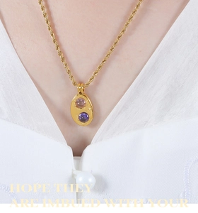 Détail du collier ovale doré avec gemmes roses et violettes et chaîne torsadée