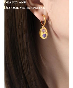 Gros plan détaillé de boucles d'oreilles ovales dorées avec zircons rose et violet portées