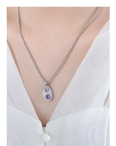 Gros plan d'un collier chaîne torsadée avec pendentif ovale et zircons roses et violets