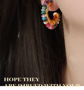 Detail of colorful gemstone beads on gold C-shaped hoop earrings worn by a model