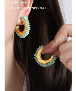 Detailed close-up of C-shaped gold earrings featuring light green beaded accents