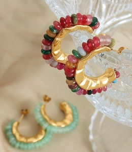 Detail of C-shaped gold plated earrings with colorful natural stones on warm fabric