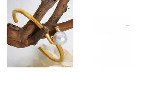 Vue détaillée d'un bracelet ouvert doré orné d'une perle blanche sur une branche naturelle