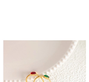 Detail of vintage gold rings featuring oval red and green gemstones on white ceramic