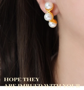 Macro view of gold plated earrings featuring triple white pearls in a sleek S-shaped design
