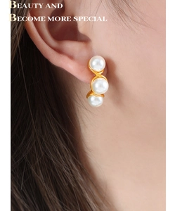 Three pearls vertically aligned on gold wave design earrings worn by a model