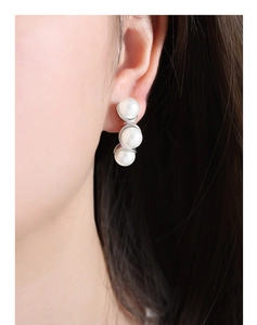 Close-up of wave-shaped silver earrings with three vertical white pearls on a model