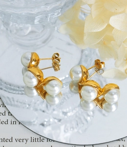 Detail of elegant gold triple pearl earrings arranged on a reflective mirror surface