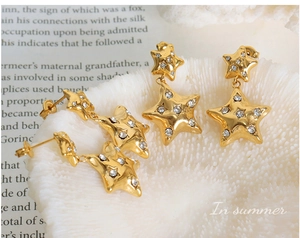 Detail of 18k gold plated star drop earrings with sparkling rhinestones on coral base