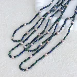 Lapis lazuli and freshwater pearl beaded necklace displayed on a white textured dish
