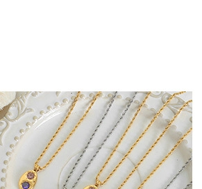 Detail view of 18k gold and silver necklaces with oval gemstone pendants on a ceramic plate