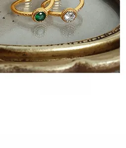 Detail view of two gold-plated rings with emerald green and white zircon stones