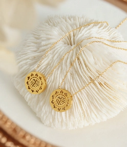 Detailed close-up of hollow gold-plated Fu pendant necklace on a decorative white coral stand