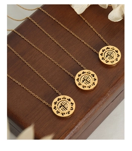 Detailed view of three gold Fu character pendant necklaces on dark wood with dry flowers