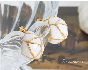 Gros plan sur des boucles d'oreilles C dorées avec motif de grille en émail blanc