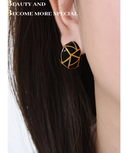 Détail de boucles d'oreilles C en émail noir avec texture géométrique dorée sur l'oreille