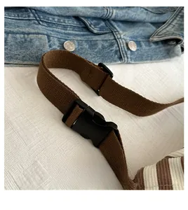 Detail of wide woven brown shoulder strap with black buckle on striped canvas crossbody bag