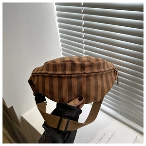 Detail of striped corduroy waist bag with adjustable strap on a minimalist desk