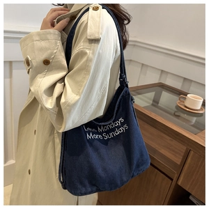 Detail of embroidered 'Less Mondays More Sundays' text on blue denim tote bag surface