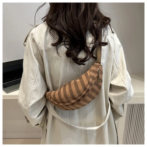 Detail of striped corduroy crescent bag with wide strap and metal zipper on trench coat