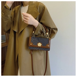 Detail of blue embossed fabric crossbody bag with floral gold lock and brown trim