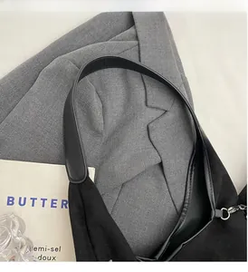 Détail du sac cabas en daim noir minimaliste avec anse en cuir sur un costume gris